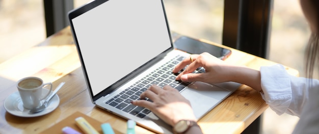 Cerrar vista de joven estudiante universitaria escribiendo en la computadora portátil en la cafetería.