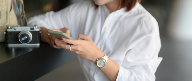 Cerrar vista de joven fotógrafa trabajando con teléfono inteligente y cámara