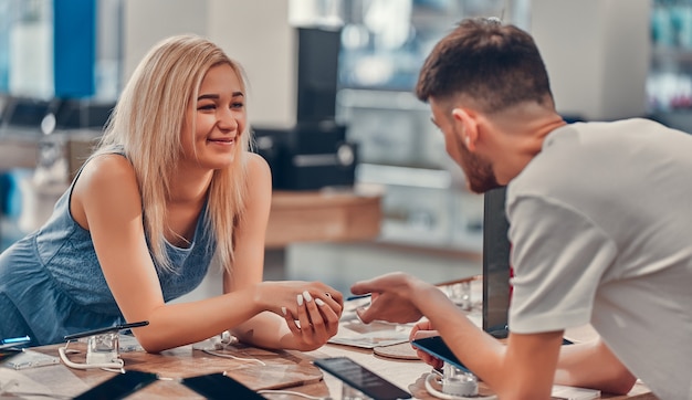 Cerrar vista lateral de pareja de amor joven inconformista emocionado bastante feliz probando nuevos dispositivos inteligentes en una tienda de tecnología.