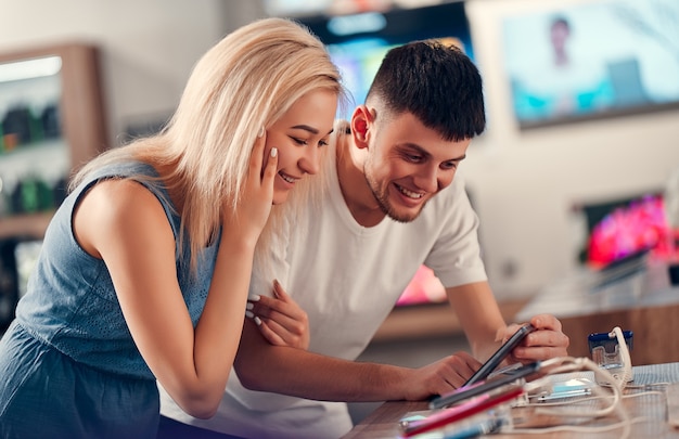 Cerrar vista lateral de pareja de amor joven inconformista emocionado bastante feliz probando nuevos dispositivos inteligentes en una tienda de tecnología.