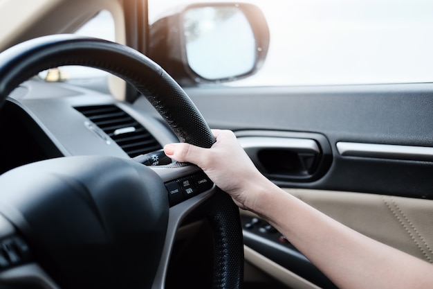 Cerrar vista de manos de mujer sosteniendo el volante conduciendo un coche en las calles de la ciudad.