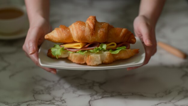 Cerrar vista de una niña desayunando, sosteniendo un plato de sandwich de croissant