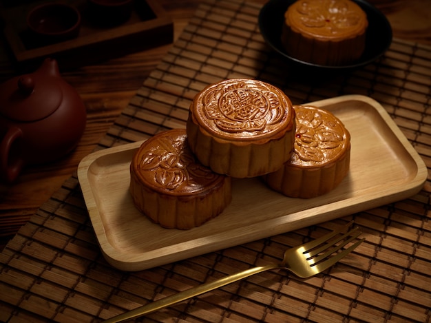 Cerrar vista de pasteles de luna tradicionales en placa de madera con tenedor y juego de té. El carácter chino en el pastel de luna representa "cinco almendras y cerdo asado" en inglés