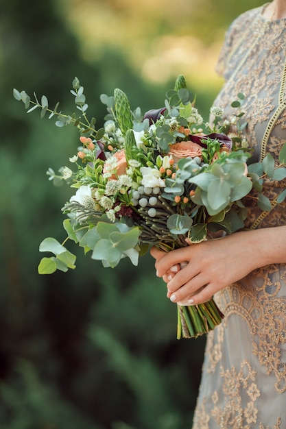 Cerrar vista de ramo de boda colorido hermoso en una mano de una novia contra el bokeh verde del fondo de la naturaleza