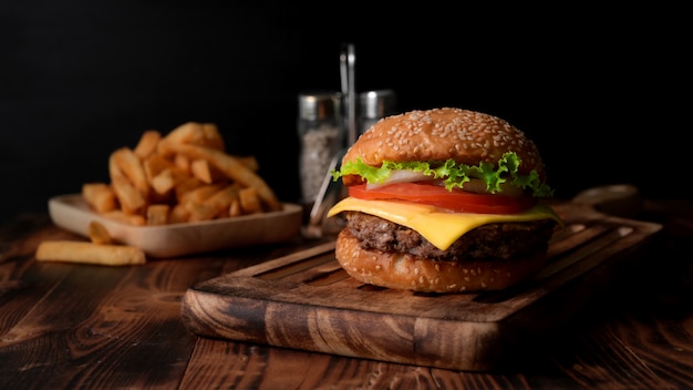 Cerrar vista de sabrosa hamburguesa fresca en bandeja de madera y papas fritas