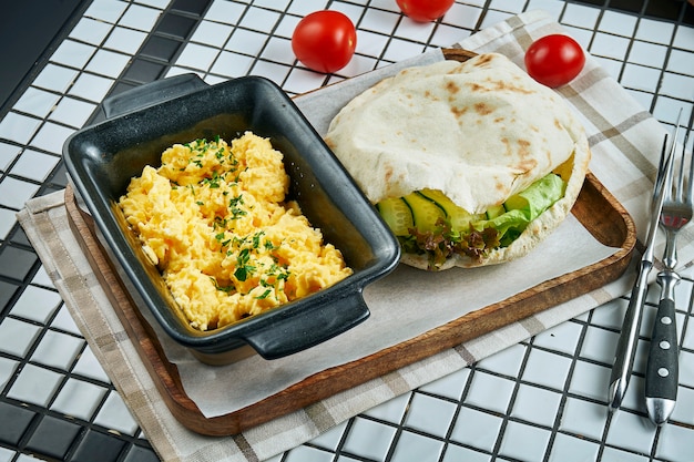 Cerrar vista sobre delicioso desayuno: huevos revueltos con verduras con pan de focaccia servido en pergamino sobre mesa blanca.