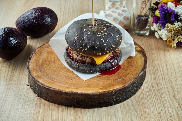 Cerrar vista sobre sabrosa, jugosa hamburguesa con un bollo negro con queso y carne, salsa de arándanos y carne sobre una tabla de madera.