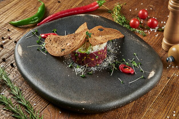 Cerrar vista sobre tartar de carne fresca con pan, huevo y microverde en plato blanco. Ternera tartare casera en superficie de madera con espacio de copia. Comida servida para menú o receta. Aperitivo de cocina italiana