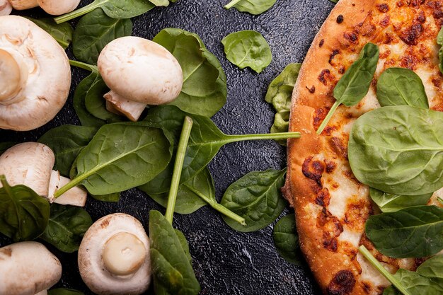 Cerrar vista superior de pizza cubierta con hojas de espinacas junto a champiñones sobre fondo de madera oscura.