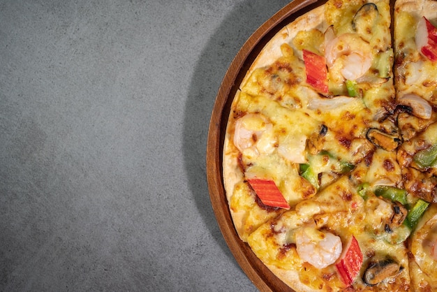 Cerrar la vista superior de sabrosos mariscos horneados calientes pizza crujiente mejillones camarones y kani con ají y queso mozzarella derretido en masa de pizza redonda en una bandeja de pizza de madera sobre textura de hormigón