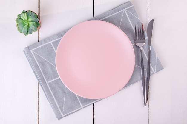 Cerrar la vista superior de servir plato rosa vacío, cuchillo y tenedor en una servilleta de lino doblada con patrón geométrico. Enfoque selectivo. Maqueta, espacio de copia, minimalismo.
