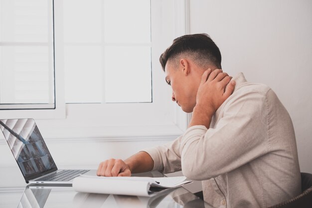 Cerrar vista trasera estresado joven tocando la parte inferior del cuello sintiendo malestar, sufriendo de dolor repentino debido al estilo de vida sedentario o al exceso de trabajo de la computadora en una postura incorrecta en la oficina en casa.