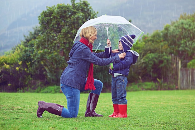 Foto certificando-se de que ele está coberto foto de corpo inteiro de uma mãe certificando-se de que seu filho esteja coberto enquanto estiver fora na chuva