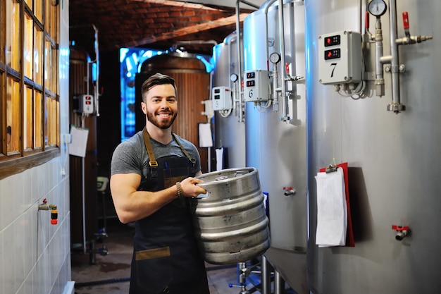 Cervecero masculino con barril de cerveza metálico.