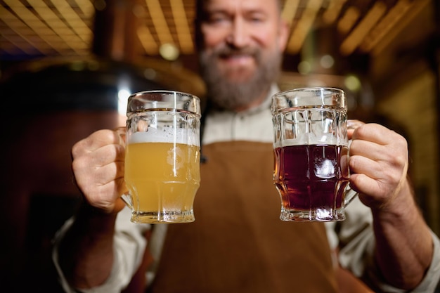 Cervecero senior satisfecho posando para la cámara con cerveza pálida y pinta de cerveza oscura