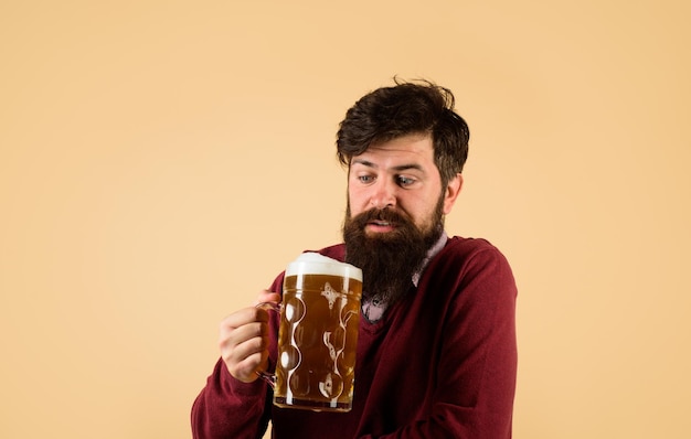 El cervecero sorprendido sostiene un vaso con cerveza. Guapo hombre barbudo bebiendo cerveza. Celebración del festival de oktoberfest. Concepto de cervecería. Hombre degustando cerveza de barril. Cervecería y bar. El hombre sostiene una taza de bebida.