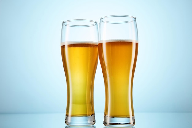 Cerveja amarela efervescente derramada em copos altos em azul claro