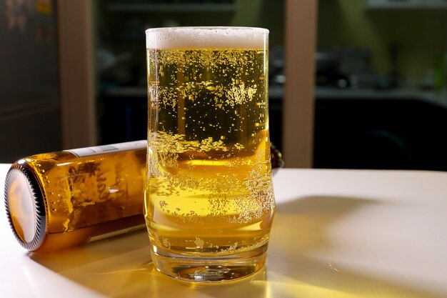 Cerveja de cerveja pilsen com espuma no vidro no branco de madeira da barra contrária com garrafa de cerveja.