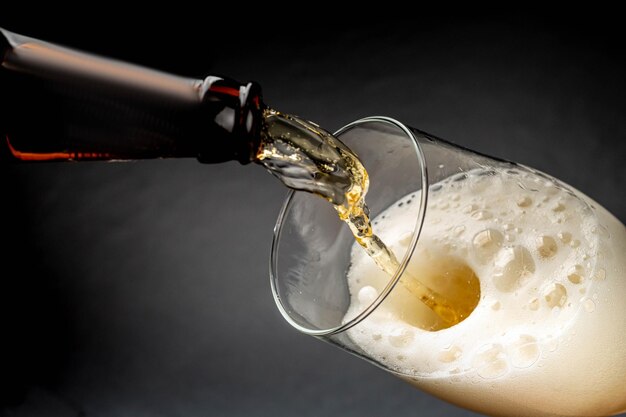 Foto cerveja derramando em um copo com espuma em um fundo escuro