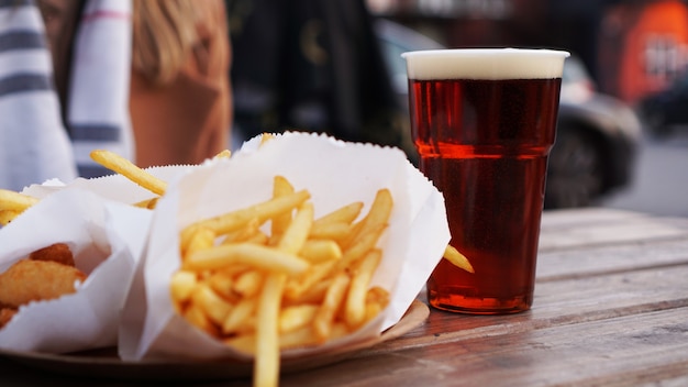 Cerveja escura e batata frita em mesa de madeira com comida para viagem na praça de alimentação