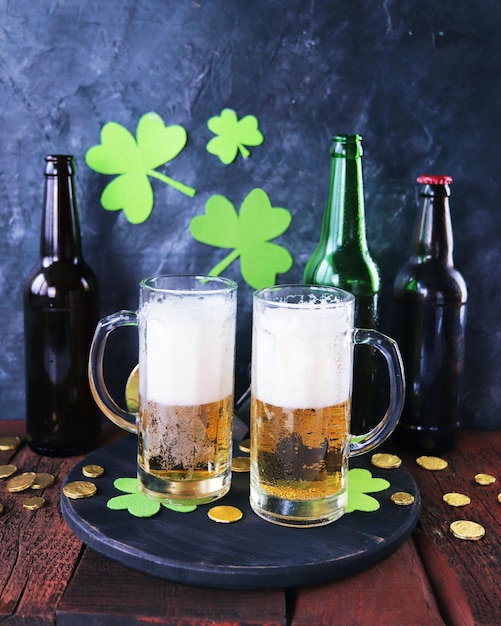 Cerveja fresca de St Patricks Day em canecas de vidro e uma garrafa de moedas de ouro em uma mesa de madeira vermelha
