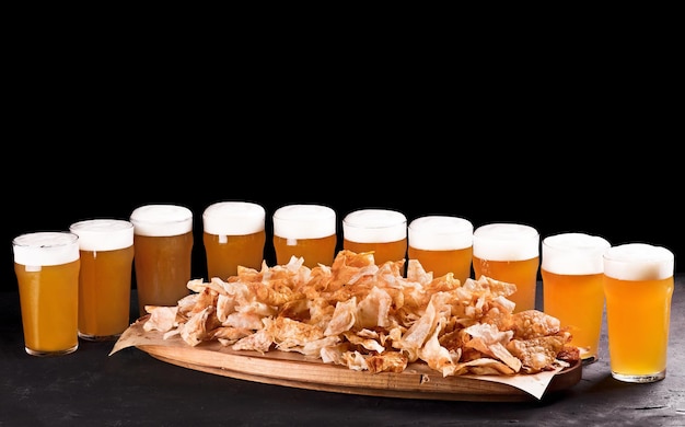 Cerveja para um grande grupo de amigos Cerveja em copos closeup na mesa de concreto Cerveja e lanches são batatas fritas crocantes em uma bandeja de madeira Espaço para cópia