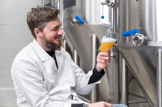 Cervejeiro vestindo jaleco branco controlando o processo de fermentação de cerveja enquanto trabalhava na fábrica de cerveja moderna