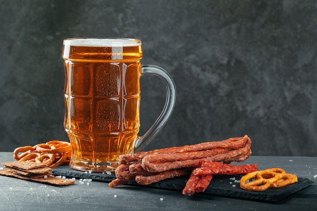 cerveza y apetitosos aperitivos de cerveza. Mesa con jarra de cerveza, tabla de madera con salchichas