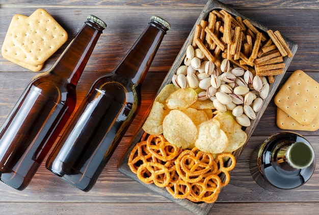 Cerveza en botellas de vidrio y snacks salados para cerveza en platos de madera. Estilo rústico. Fondo de madera marrón.