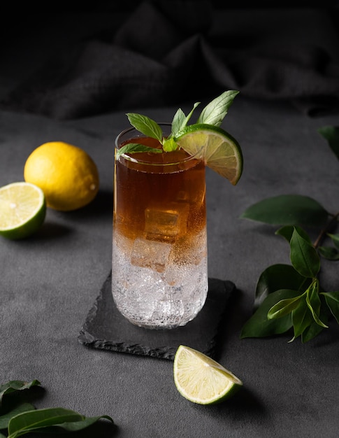 Cerveza de café con hielo tónico y limón en un vaso alto sobre un fondo oscuro con cítricos y ramas Bebida de moda refrescante conceptual