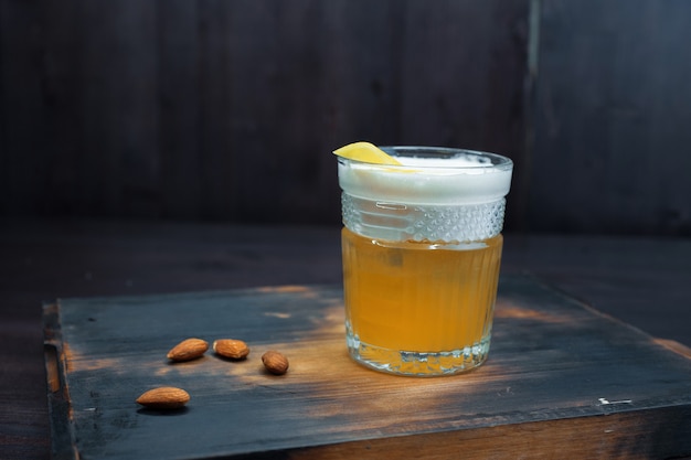 Cerveza dorada con espuma blanca en un vaso de cerveza está de pie sobre una mesa de madera negra en el bar. La bebida está decorada con cacahuetes. Se sirve frío. Disfruta el fin de semana