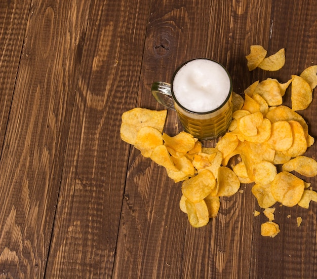 La cerveza espumosa con patatas fritas crujientes en la mesa.