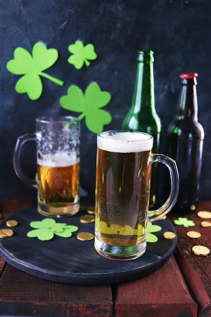 Cerveza fresca del día de San Patricio en tazas de vidrio y una botella de monedas de oro en una mesa de madera roja