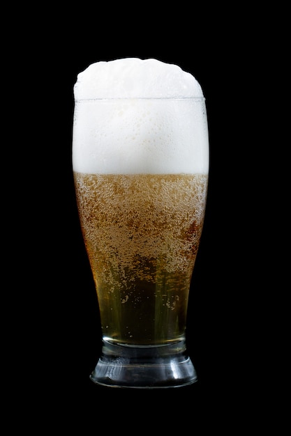 Cerveza fría con espuma en un vaso sobre un fondo negro.