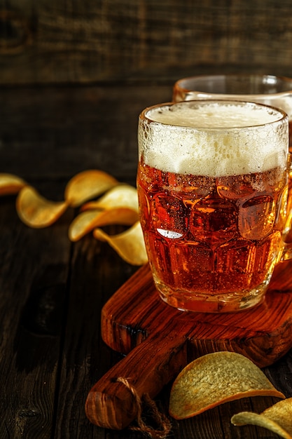 Cerveza fría en vaso con patatas fritas en una mesa oscura.