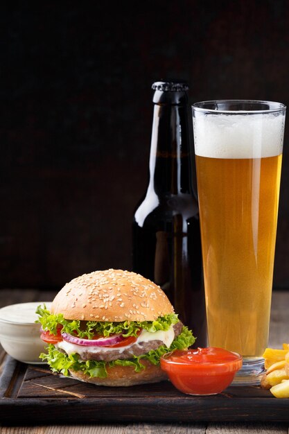 Cerveza de hamburguesa en una botella y en un vaso de salsa de papas fritas en un concepto de comida rápida de fondo oscuro