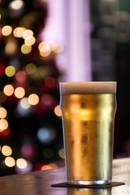 de cerveza lager pilsner en un mostrador de un pub decorado para Navidad con un árbol borroso en el fondo y luces parpadeantes