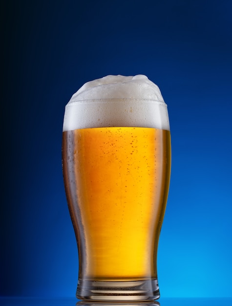 Cerveza ligera con espuma blanca en vidrio sobre azul