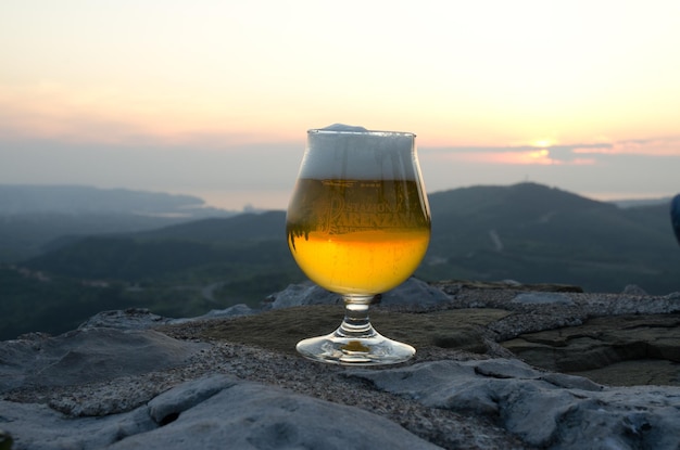 Cerveza ligera con espuma en un vaso se encuentra en el borde de una colina contra el cielo del atardecer de cerca. Vista superior.