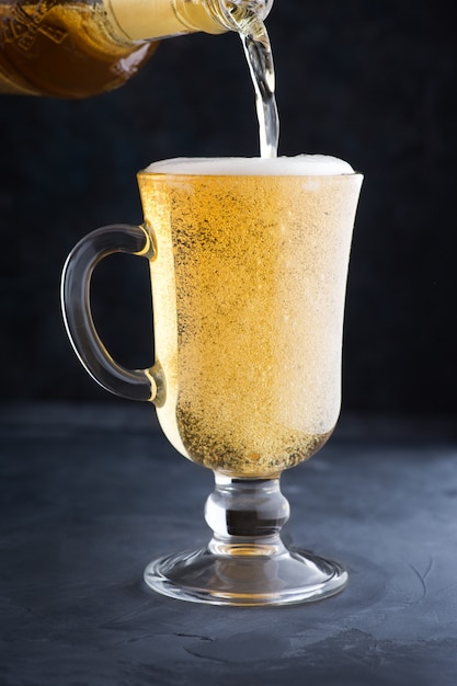 Cerveza ligera refrigerada con espuma en una taza de vidrio vertiendo cerveza en un vaso en el mostrador del bar o pub