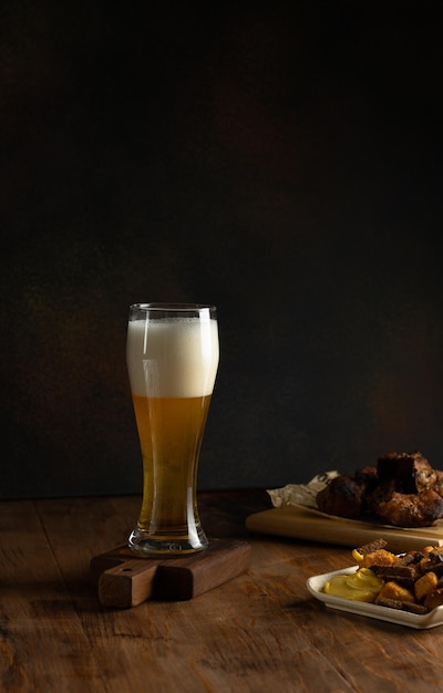 Cerveza ligera en un vaso alto, bocadillos de cerveza, carne a la parrilla en una mesa de madera sobre un fondo oscuro, primer plano