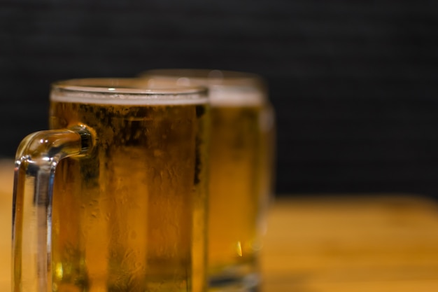 Cerveza en taza de vidrio con hielo y espuma en una mesa de madera