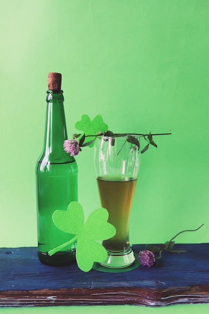 Foto cerveza en un vaso y en una botella flores frescas de trébol sobre un fondo verde día de san patricio