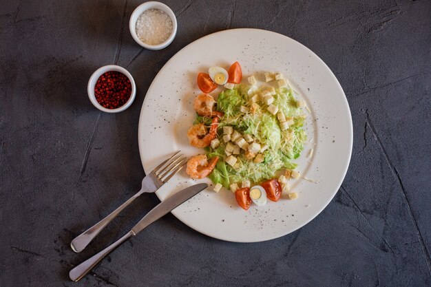 Cesar Salat mit Garnelen, frisch und lecker. Weißer Teller mit Salat auf dem grauen Hintergrund.