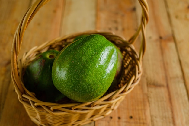 Cesta con aguacates en mesa de madera