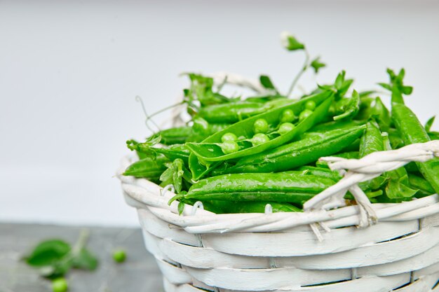 Cesta branca com ervilhas verdes frescas na mesa cinza.