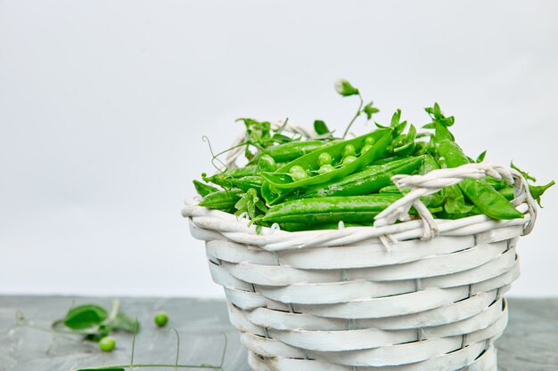 Cesta branca com ervilhas verdes frescas na mesa cinza.