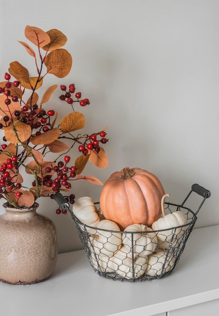 Cesta con calabazas, hojas de otoño y ramo de bayas en un jarrón, una sencilla decoración otoñal sobre la mesa