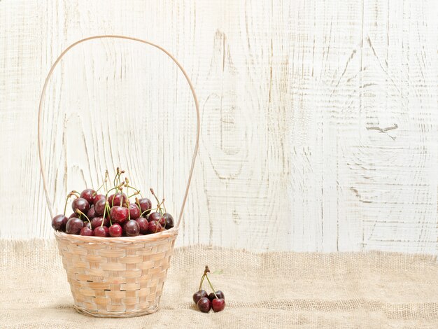 Cesta com alça e cerejas em uma mesa de madeira. Copie o espaço