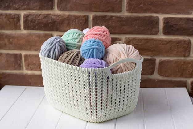 Cesta com bobinas de fios de pelúcia em cores pastel A cesta de Knitter em uma mesa branca